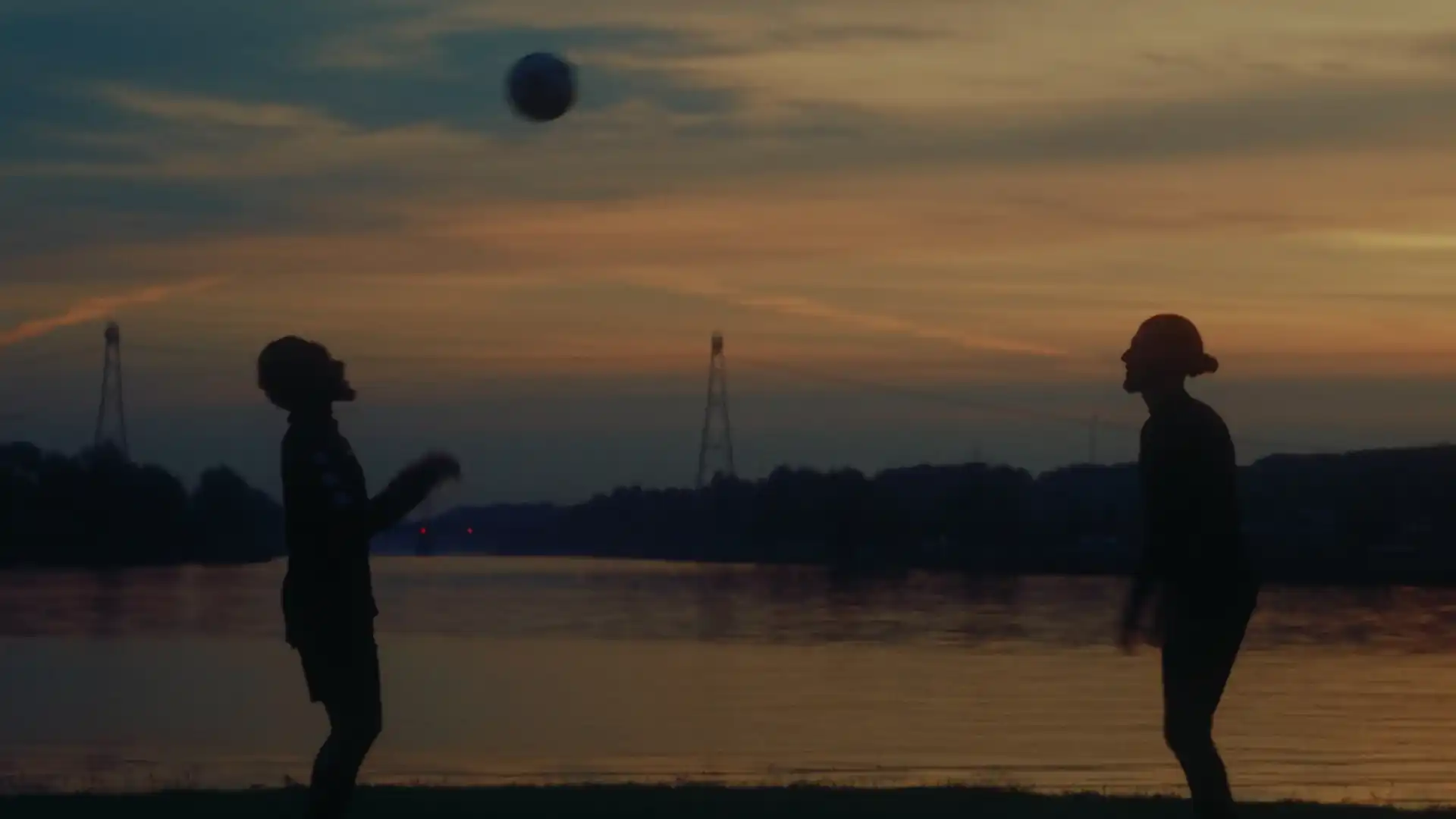Twee spelers koppen een bal over bij zonsondergang aan het water